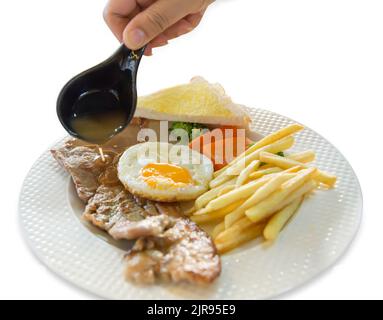 Stempelschnitt von Soße auf Schweinefleisch Steak mit pommes frites, Spiegeleier, Toast auf weißem Teller, auf weißem isoliert. Stockfoto