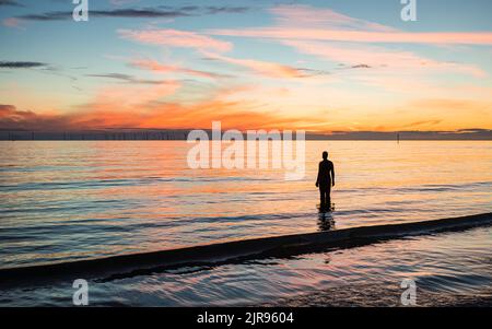 Eine Silhouette einer Iron man Statue bei Sonnenuntergang am Crosby Beach in der Nähe von Liverpool mit Blick auf die Irische See im August 2022. Stockfoto