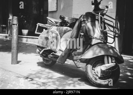 Eine Aufnahme der italienischen Vespa, die auf der Straße geparkt wurde, in niedrigen Graustufen Stockfoto