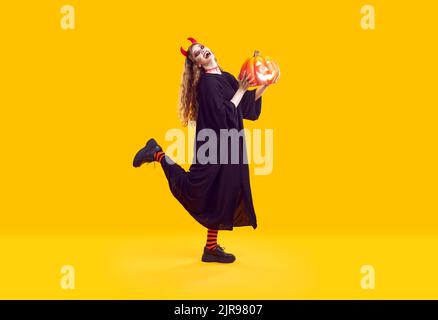 Emotionale Frau gekleidet als verrückter Teufel für Halloween-Feier isoliert auf orangefarbenem Hintergrund. Stockfoto