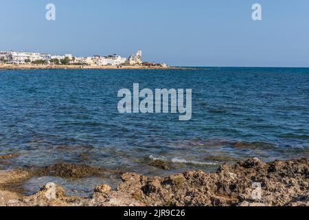 Panoramablick auf Torre San Giovanni und seine felsige Küste, mit Leuchtturm im Hintergrund, Marina di Ugento, Salento, Apulien, Italien Stockfoto