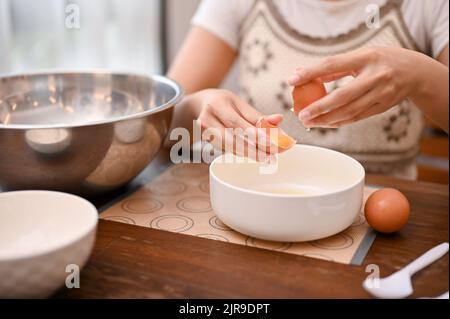 Ein Weibchen knackt ein Ei und trennt Eigelb vom Eiweiß, bereitet die Cupcake-Zutaten in der Küche zu. Zugeschnittenes Bild Stockfoto