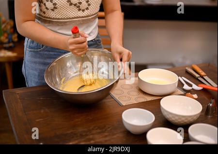 Eine Frau macht einen hausgemachten Cupcake in ihrer Küche und bringt ihre weiche Butter, Zucker, Eier und Mehl in der Rührschüssel zusammen. Zugeschnittenes Bild Stockfoto