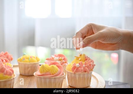 Kurzer Cupcake-Schuss mit einer Frau, die den Cupcake in der Küche von Hand schmückte Stockfoto