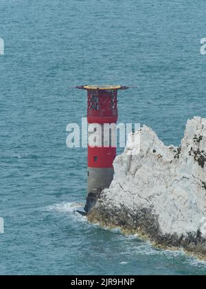 Der Leuchtturm an den Needles in einem stählernen Meer und hinter zackigen, zahnartigen Aufschlüssen, die deutlich machen, warum das Leuchtfeuer benötigt wird. Stockfoto