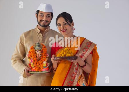 Portrait des Maharashtrian Paares, das die Statue von Lord Ganesh und einen Teller mit süßem Essen trägt Stockfoto