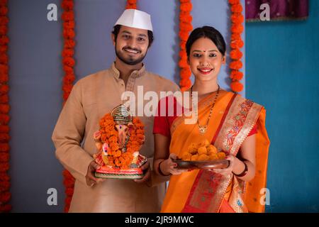 Portrait des Maharashtrian Paares, das die Statue von Lord Ganesh und einen Teller mit süßem Essen trägt Stockfoto