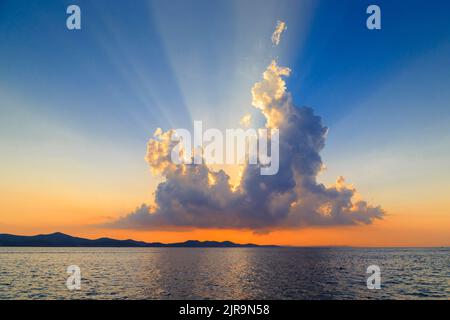 Die Strahlen der Sonne, die bei Sonnenuntergang hinter einer Sonnenwolke untergeht, beleuchten diese Wolke ungewöhnlich. Stockfoto