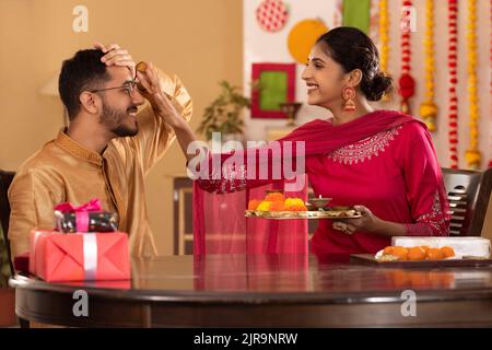 Schwester, die anlässlich von Raksha Bandhan tika auf die Stirn ihres Bruders applyte Stockfoto