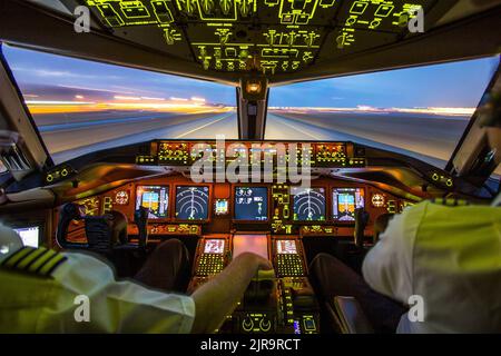 Airliner-Cockpit mit einem Piloten und einem Co-Piloten und einer Landebahn, die nachts vom Innenraum aus betrachtet wird Stockfoto