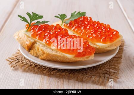 Zwei Sandwiches mit rotem Kaviar auf einer Untertasse über einem Holztisch. Gourmet-Vorspeise mit Forellenkaviar auf einer französischen Baguette-Scheibe mit Butter. Nahaufnahme. Stockfoto