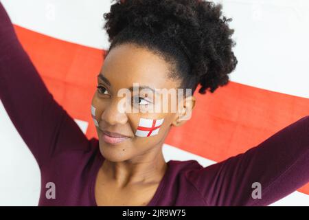 Bild einer glücklichen afroamerikanischen Frau mit Flaggen englands auf dem Gesicht über der Flagge englands Stockfoto