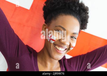 Bild einer glücklichen afroamerikanischen Frau mit Flaggen englands auf dem Gesicht über der Flagge englands Stockfoto