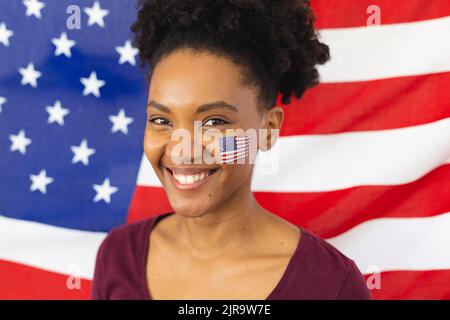 Bild einer glücklichen afroamerikanischen Frau mit Flaggen der usa auf dem Gesicht über der Flagge der usa Stockfoto