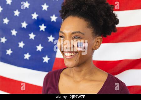 Bild einer glücklichen afroamerikanischen Frau mit Flaggen der usa auf dem Gesicht über der Flagge der usa Stockfoto