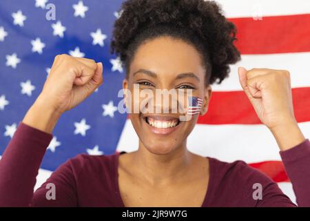 Bild einer glücklichen afroamerikanischen Frau mit Flaggen der usa auf dem Gesicht über der Flagge der usa Stockfoto