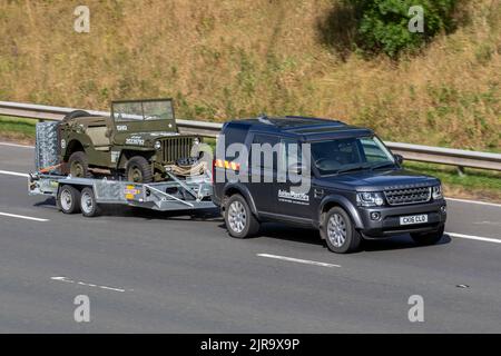 1945, vierziger Jahre, 40s Ford Jeep 2200cc Benzin; Militärfahrzeuge; 2. Weltkrieg, 2. Weltkrieg, 2. Weltkrieg, WW2. Militärfahrzeug auf Anhänger, das von Land Rover Discovery SDV6 Commercial SE abgeschleppt wird; unterwegs auf der M6 Motorway UK Stockfoto