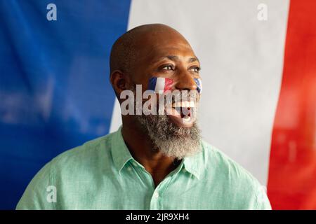 Glücklicher älterer afroamerikanischer Mann, der mit der Flagge frankreichs und des Fußballs sitzt Stockfoto