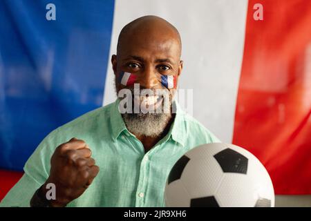 Porträt eines glücklichen älteren afroamerikanischen Mannes, der mit der Flagge frankreichs und des Fußballs sitzt Stockfoto