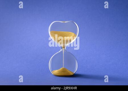 Sandglas, auch Sandglas oder Sanduhr genannt, golden auf blauem Papierhintergrund. Stockfoto