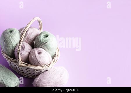 Pinke und grüne Fadenkugeln in einem Korb auf einem rosa Hintergrund zum Stricken warmer Kleidung und Hobbys Handarbeiten Stockfoto
