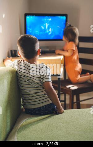 Rückansicht eines Jungen, der mit seiner Schwester auf dem Sofa sitzt und einen Cartoon am Computer sieht. Moderne Technologie. Kinder intelligente Technologie Gadget Nutzung Stockfoto