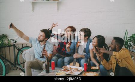 Fröhliche Studentenfreunde, die Selfie machen und posieren, während sie mit Bier und Pizza in einer Gemeinschaftsunterkunft feiern Stockfoto