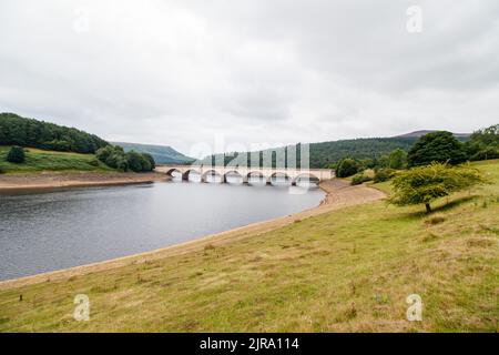 Der Ladybower Stausee während des trockenen und trockenen Wetters im Sommer 2022. Das Bild zeigt den Blick auf die Brücke von Ashopton, wo sich die A57 kreuzt, die Markierungen auf der Brücke zeigen den üblichen Wasserstand. Ladybower Reservoir ist ein großes Y-förmiges, künstliches Reservoir, das niedrigste von drei im Upper Derwent Valley in Derbyshire, England. Stockfoto