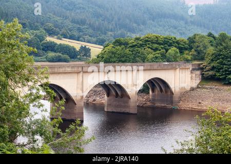 Die Ashopton Bridge auf der A57, die den Ladybower-Staudamm im Peak-Distrikt überquert.der Ladybower-Stausee während des trockenen und trockenen Wetters im Sommer 2022. Ladybower Reservoir ist ein großes Y-förmiges, künstliches Reservoir, das niedrigste von drei im Upper Derwent Valley in Derbyshire, England. Stockfoto