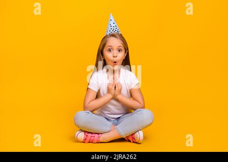 In voller Länge Foto von ziemlich beeindruckt Schulmädchen gekleidet weißen T-Shirt Geburtstag Kopfbedeckung isoliert gelbe Farbe Hintergrund Stockfoto