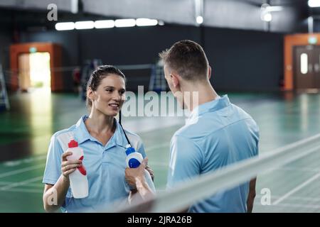 Lächelnde junge Frau, die mit einem Freund spricht, nachdem sie gemeinsam auf dem Platz Badminton gespielt hat Stockfoto
