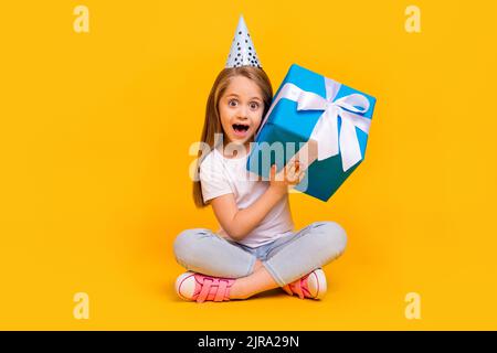 In voller Länge Foto von ziemlich lustig Schulmädchen gekleidet weißen T-Shirt Geburtstag Kopfbedeckung raten innen Geschenk isoliert gelbe Farbe Hintergrund Stockfoto