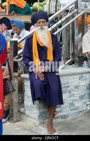 Ein blau gekleideter Sikh-Ältester sitzt vor dem Sikh Cultural Center in Richmond Hills, Queens. Vor dem Beginn der Parade von Nagar Kirtan Stockfoto