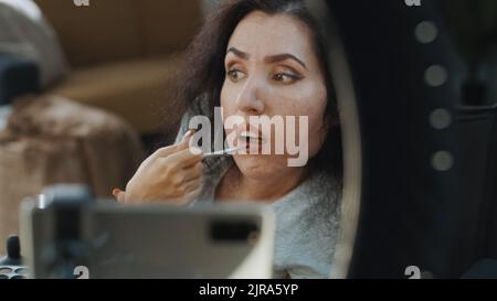 Make-up-Künstlerin mit Behinderung nimmt ein Video auf oder macht Live-Videostreams in sozialen Medien für ihren Blog im Heimstudio, mit Stativ und Ring-LED-Lampe, während sie einen Lippenstift zum Make-up aufsetzt Stockfoto