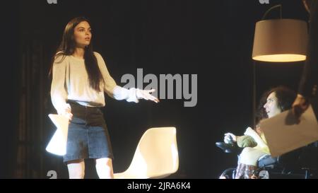 Theaterschauspieler mit einer behinderten Schauspielerin im Rollstuhl mit Drehbüchern Proben eine Szene für ein Theaterstück auf einer dunklen Theaterbühne, mit Dekorationen und beleuchtet von einem Scheinwerfer Stockfoto
