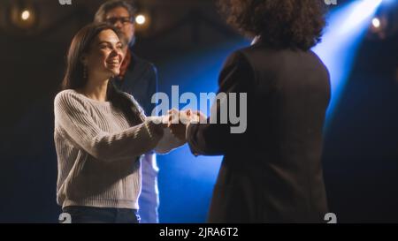 Eine Schauspielerin und ein Schauspieler probten auf einer Theaterbühne mit einem Scheinwerfer eine Liebesszene, während ein männlicher Regisseur sie beobachtete Stockfoto