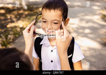 Die Mutter bereitet ihr Kind vor dem Schuleintritt vor. Er legt die Brille auf seine Augen. Stockfoto