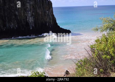 Perfekte Wellen in kristallinen Gewässern neben dem Kliff der zwei Brüder, dem Strand von Cacimba, der Insel Fernando de Noronha, Brasilien Stockfoto