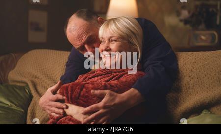 Romantisches verliebter Senioren, der sich in der Freizeit abends zu Hause umarmt und lächelt Stockfoto