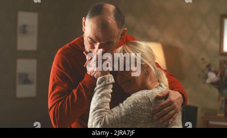 Glücklich gealterter Mann und Frau lächeln und tanzen zusammen in einem gemütlichen Wohnzimmer Stockfoto