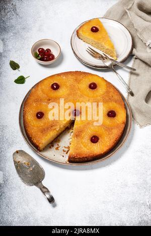Hausgemachter Ananaskuchen auf dem Kopf mit kandierten Kirschen und einem Stück auf einem Teller abgeschnitten. Tropisches Dessert im Sommer. Selektiver Fokus. Stockfoto