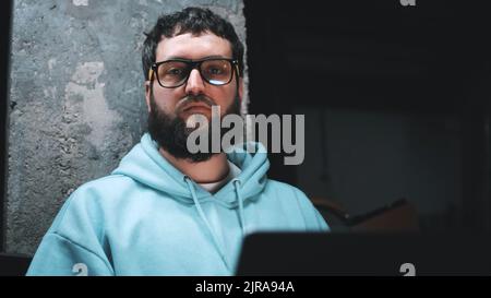 Trauriger Programmierer, der während des Krieges in einem dunklen Bombenschutzhaus auf die Kamera schaut und auf der Website arbeitet Stockfoto