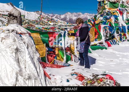 Eine Dame bindet einen Gebetsschal neben Gebetsfahnen am Yamdrok-See in Tibet-China Stockfoto