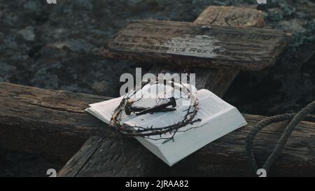 Heilige Bibel mit Dornenkrone und Nägeln auf Holzkreuz mit Schild nach Jesus Christus Kreuzigung platziert Stockfoto