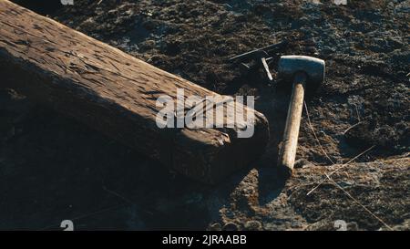 Hoher Winkel von Holzkreuz für Jesus Christus Hinrichtung auf dem Boden in der Nähe von Hammer und Nägel an windigen Tag gelegt Stockfoto