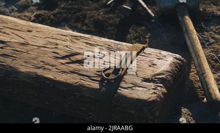 Von oben Hammer und Nägel auf dem Boden in der Nähe verwitterten Kreuz vor Jesus Christus Kreuzigung an windigen Tag gelegt Stockfoto