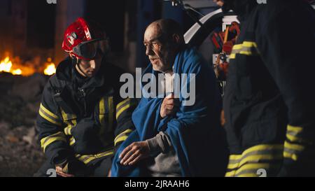 Ein Team von Rettungsassistenten bringt einen Keilrahmen aus dem Krankenwagen und hilft einem verletzten jungen Menschen. Nothelftkräfte kamen nachts am Unfallort auf einer Straße an. Stockfoto