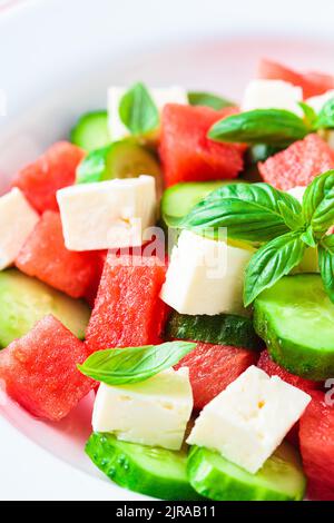 Wassermelonensalat mit Fetakäse, Gurke und Basilikum auf einem Teller, grauer Hintergrund, Nahaufnahme. Sommerrezept, gesunde Ernährung, Detox-Lebensmittel. Stockfoto