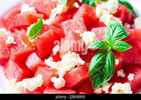 Wassermelonensalat mit Feta-Käse und Basilikum auf einem Teller, grauer Hintergrund. Sommerrezept, gesunde Ernährung, Detox-Lebensmittel. Stockfoto