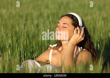 Frau mit Kopfhörern, die sich entspannt in einem Weizenfeld bei Musik anhört Stockfoto